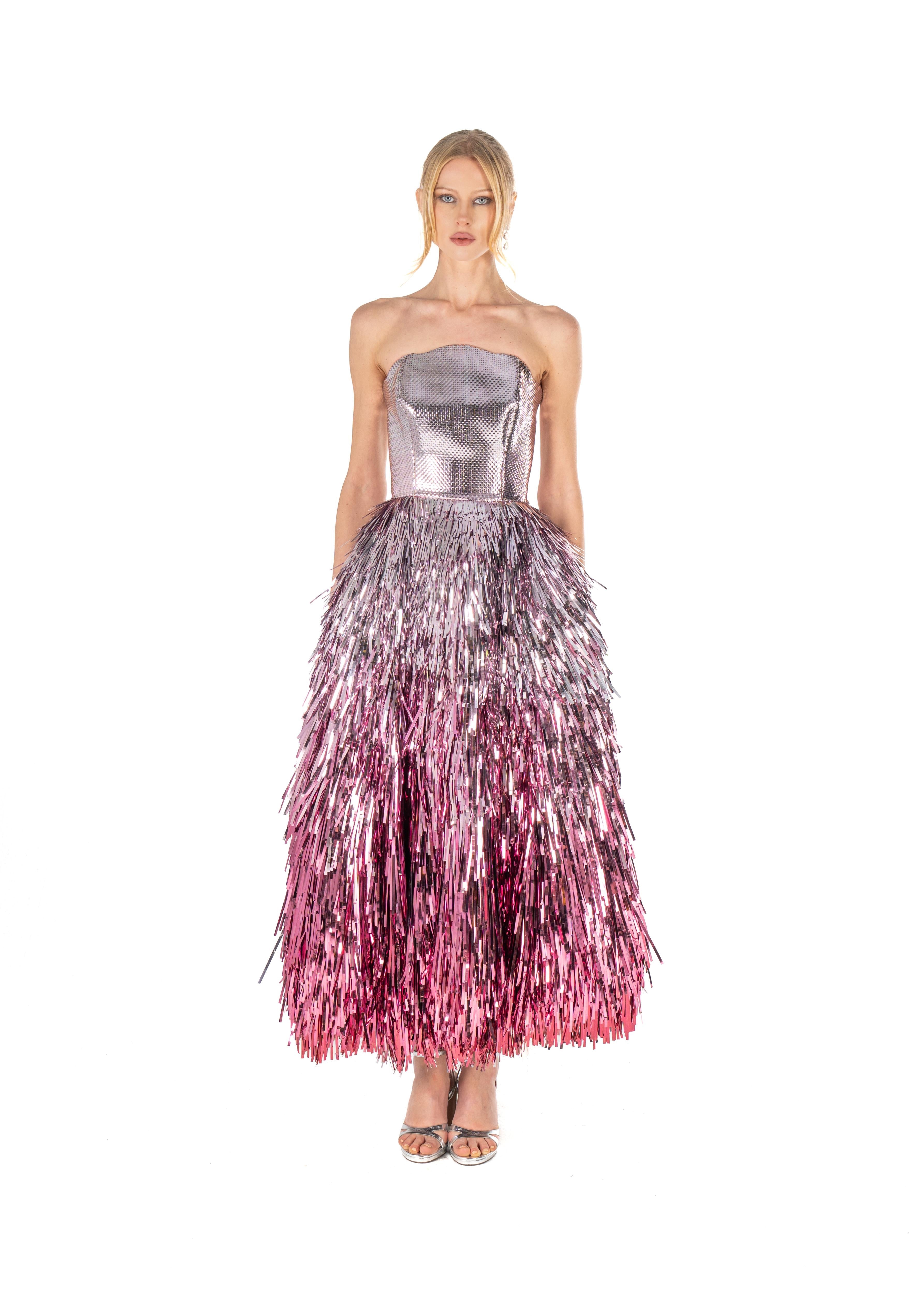 Woman wearing a silver strapless top and pink and purple fringe skirt on a white background