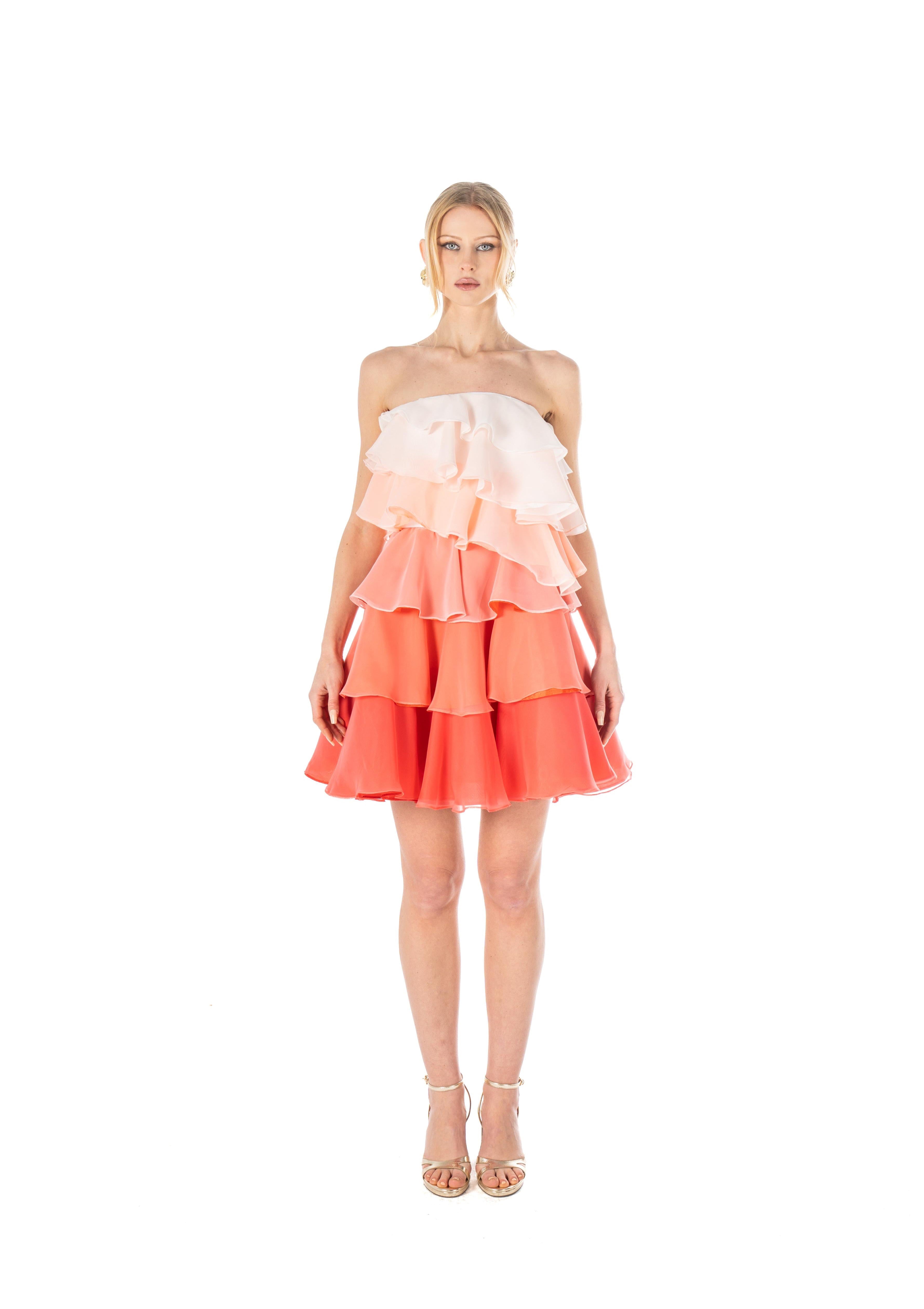 Woman wearing a strapless, tiered dress with a gradient of white to pink to red on a white background.