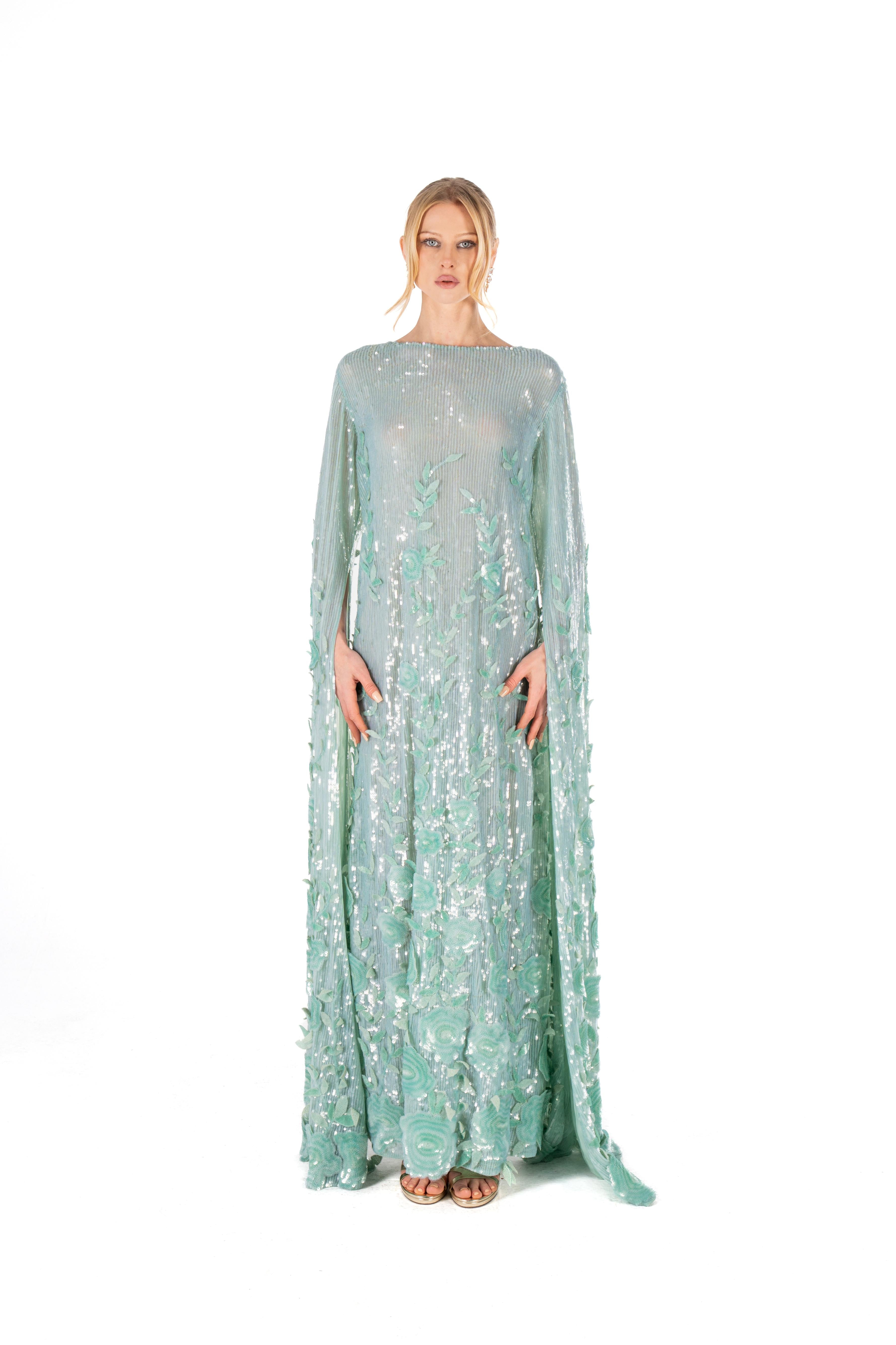 Woman wearing a light green evening gown with floral embroidery on a white background