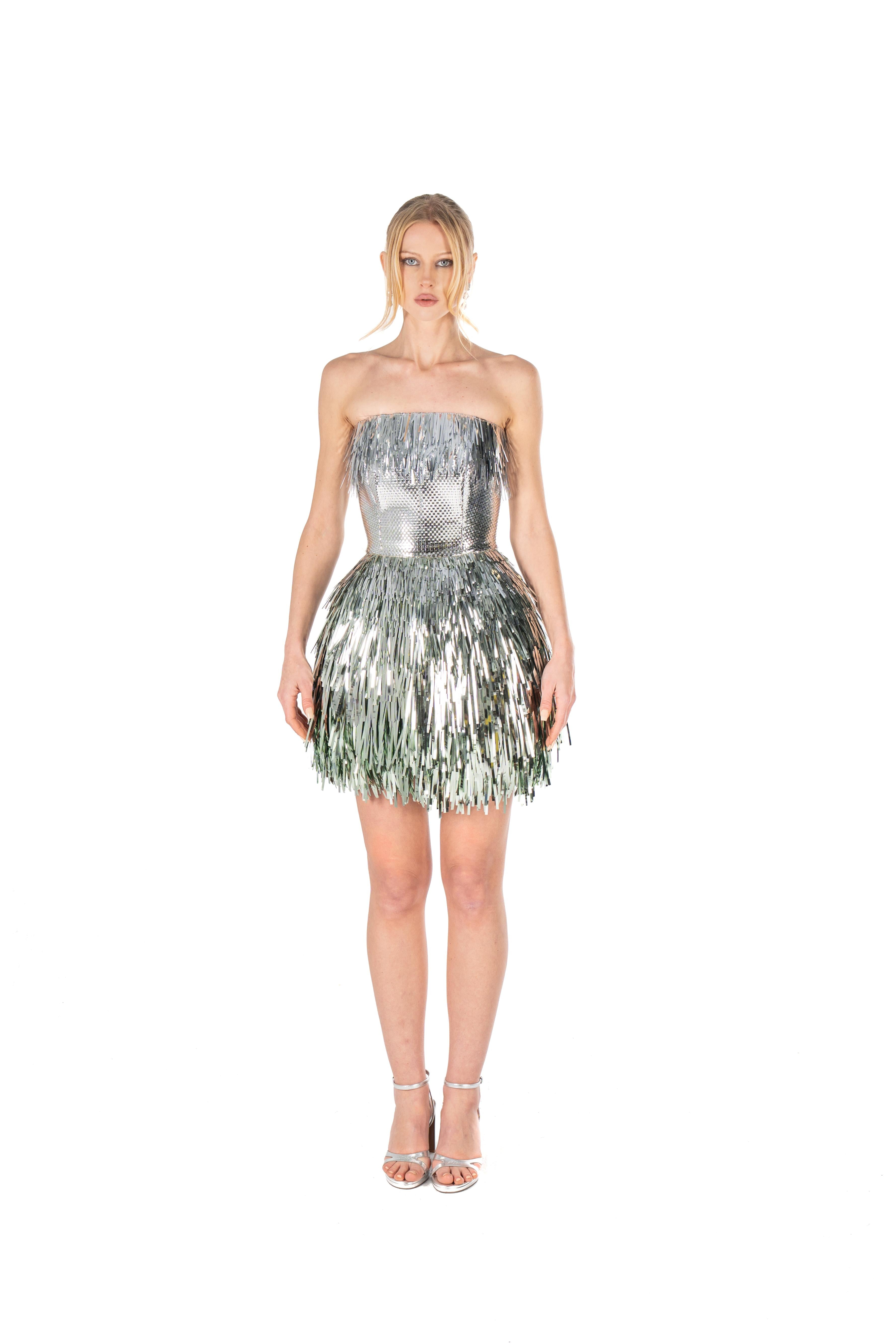 Woman wearing a silver strapless dress with fringe details on a white background